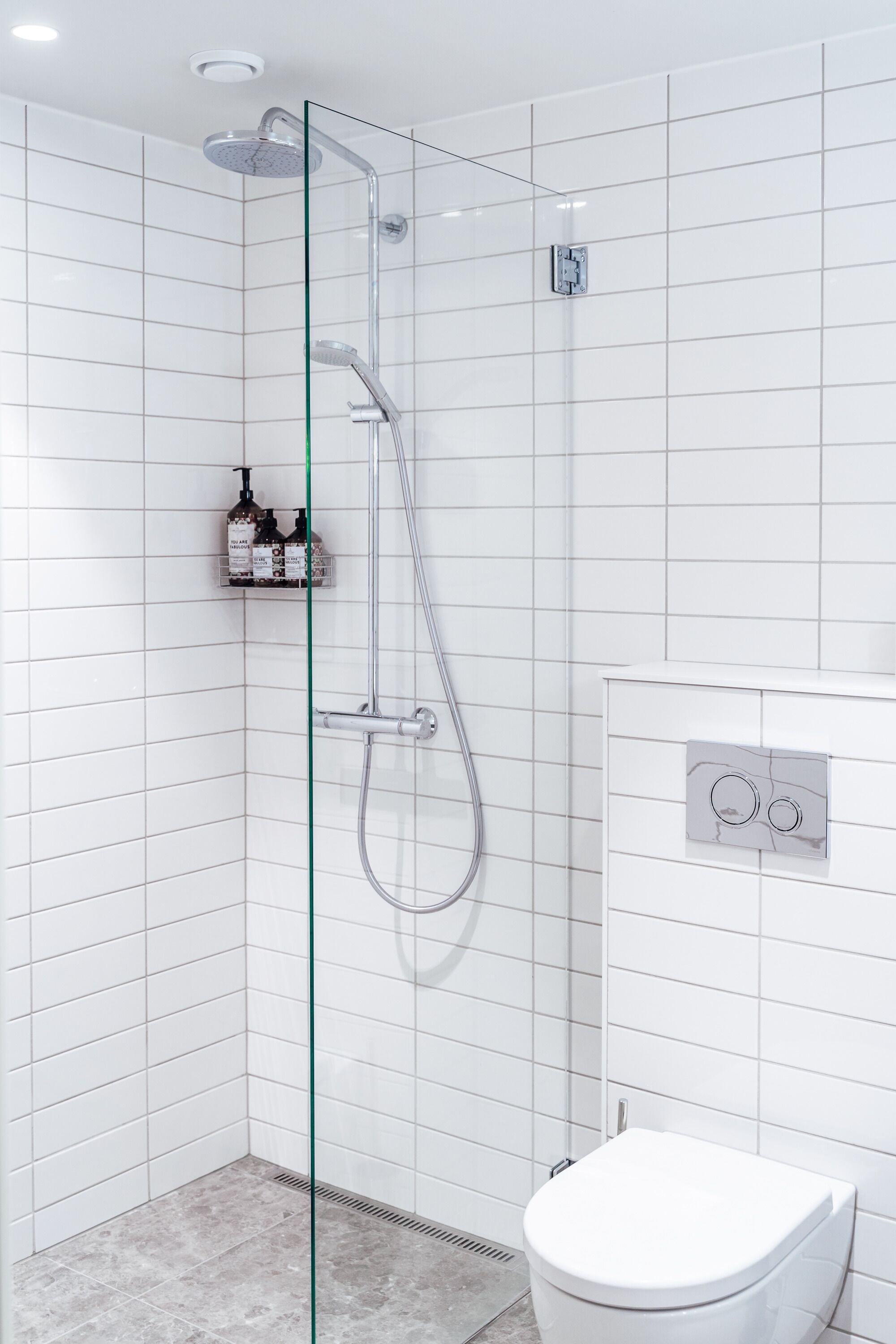 A modern bathroom with a glass-enclosed shower, a white toilet, and a wall-mounted control panel.