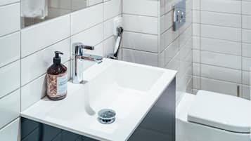 A modern bathroom with white tiles, a sink, a mirror, and a toilet.