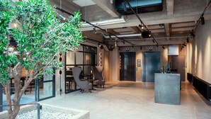 A modern office space with a large tree, seating area, and a reception desk. - Unity Tampere - A Studio Hotel (Tampere)