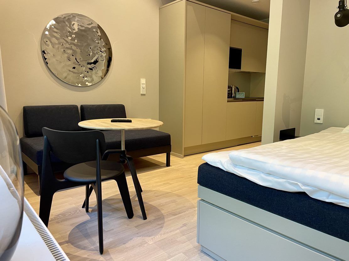 Un dormitorio moderno con una cama, una mesita redonda pequeña, un sofá y un espejo grande.
