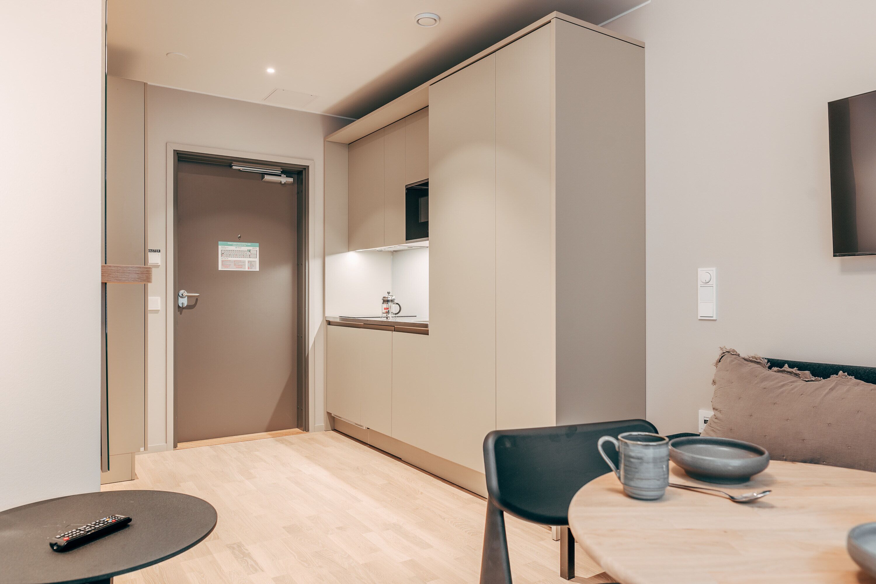 A modern kitchen with a dining area, including a table with chairs, a remote control, and a kettle.
