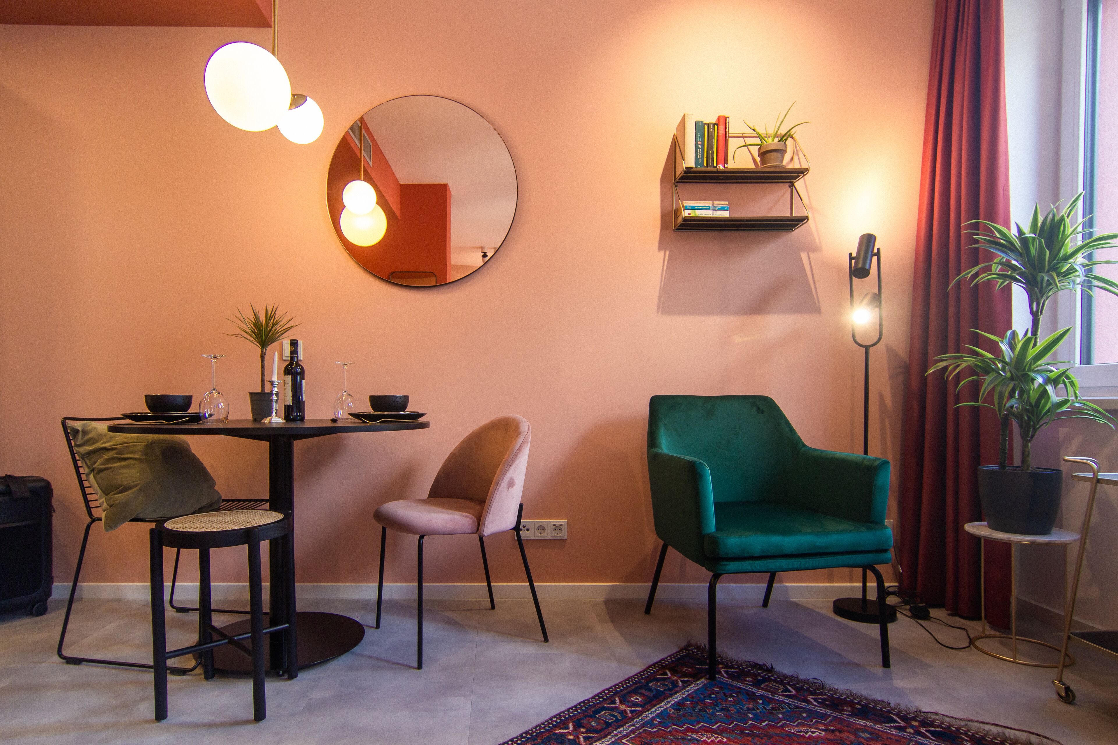 Un soggiorno moderno con uno specchio rotondo, un tavolo da pranzo con sedie, una poltrona verde, una libreria e una pianta in vaso.