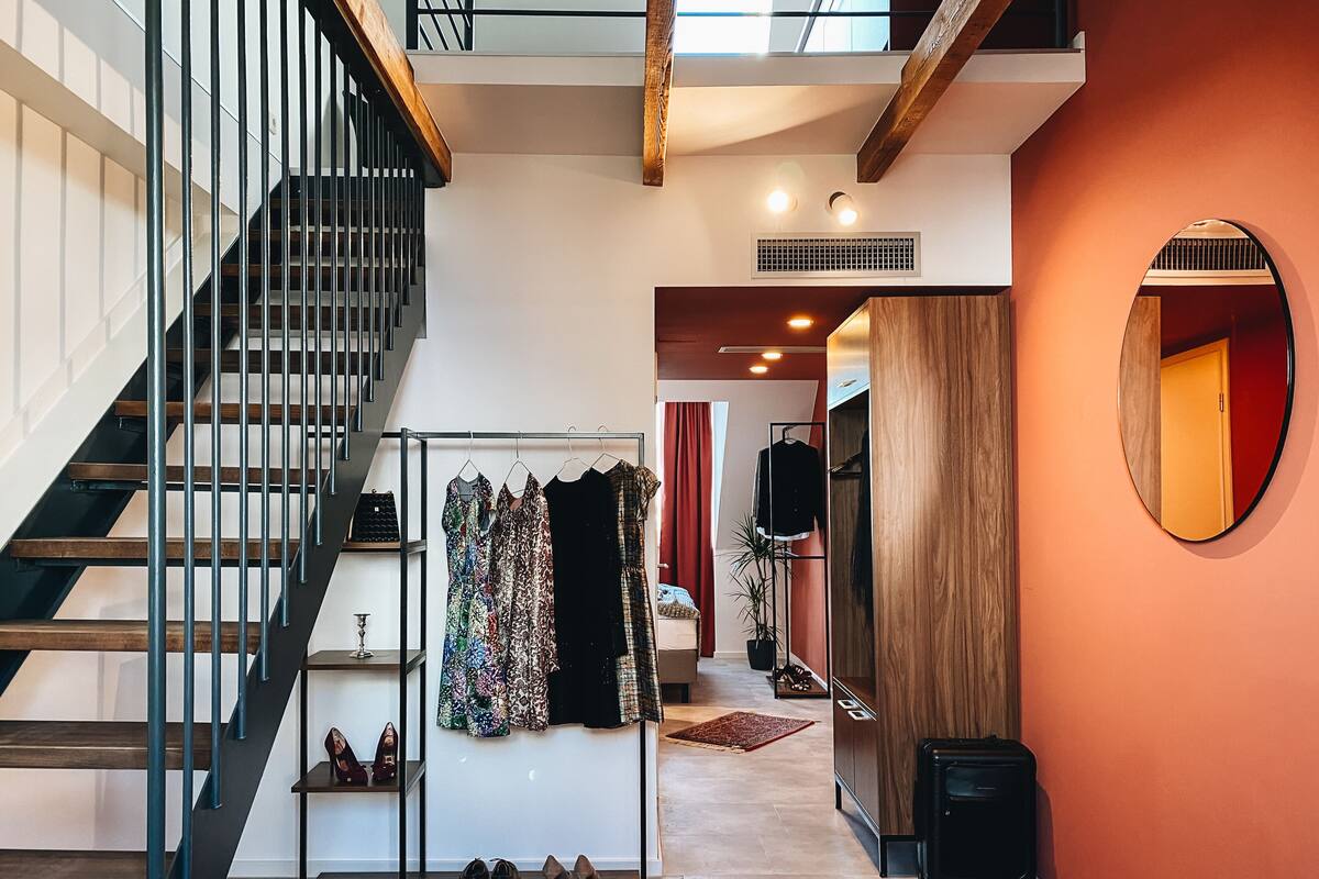 Un intérieur spacieux comprenant un escalier, un portant à vêtements, un miroir et une valise.