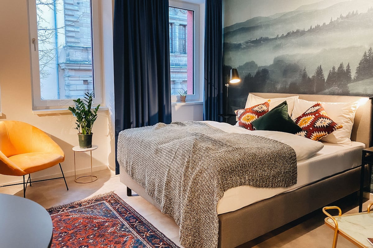 Une chambre à coucher moderne avec un lit, une chaise, un tapis et une vue sur un immeuble par la fenêtre.