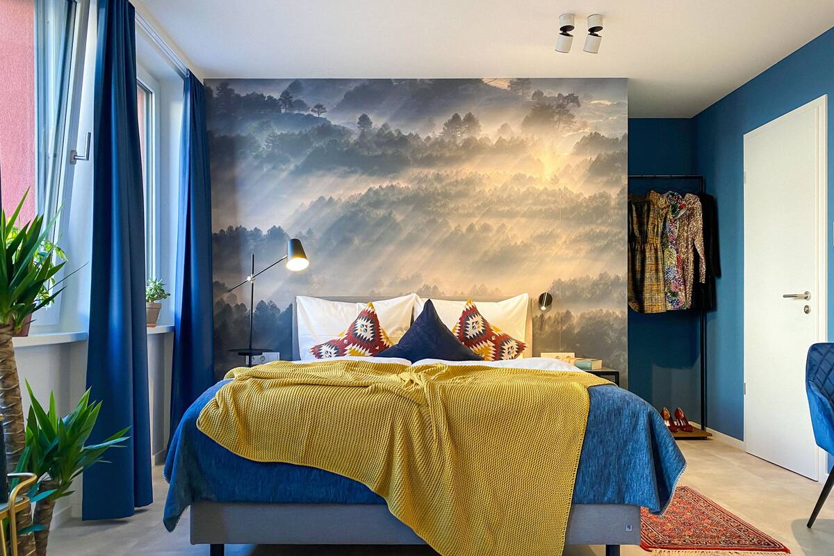 Une chambre à coucher moderne avec un lit, une table de chevet, une lampe et une grande fresque murale.
