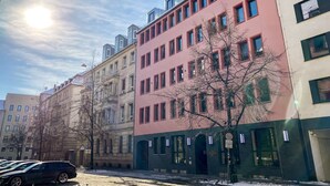 A row of multi-story buildings with a mix of architectural styles, including a pink building with a dark facade and a beige building with a light facade. - Astoria Apartments (Nuremberg)