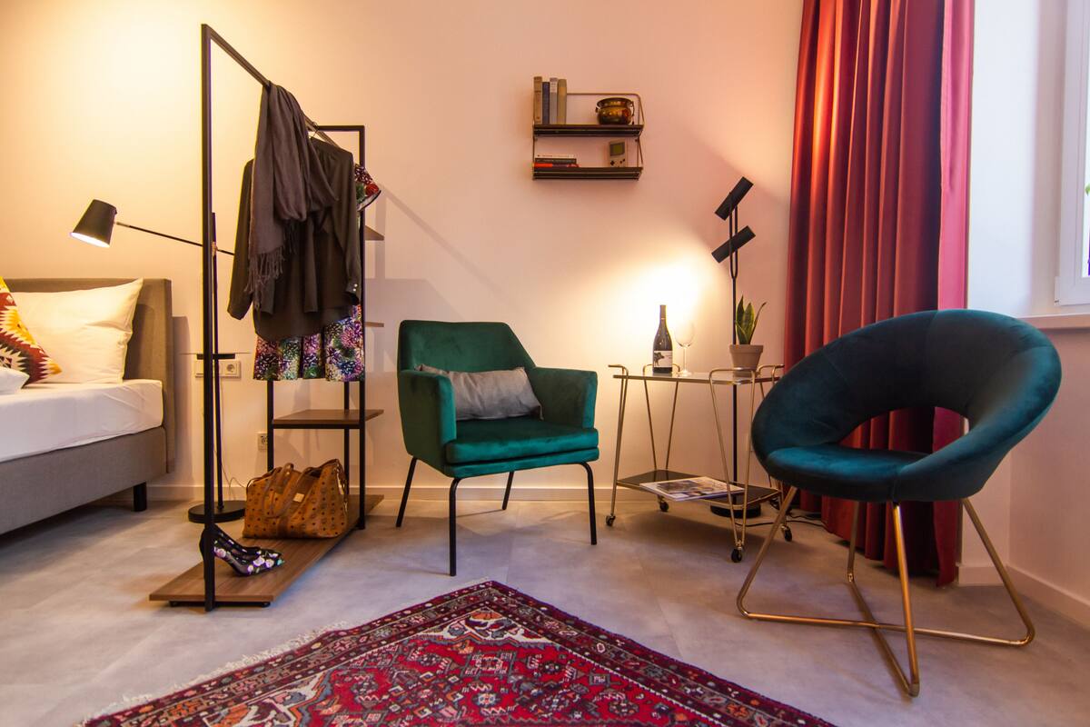 Un salon moderne avec un canapé, un fauteuil vert, une petite table avec une bouteille et des verres, et un rideau rouge.