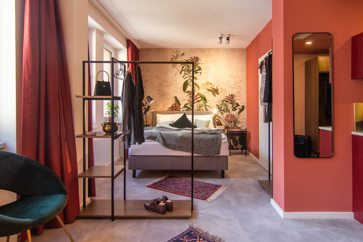 Une chambre moderne avec un lit, une étagère où sont rangés des vêtements, une chaise et un miroir.