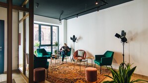A modern interior with a large window, green chairs, a patterned rug, and a potted plant. - Astoria Apartments (Nuremberg)