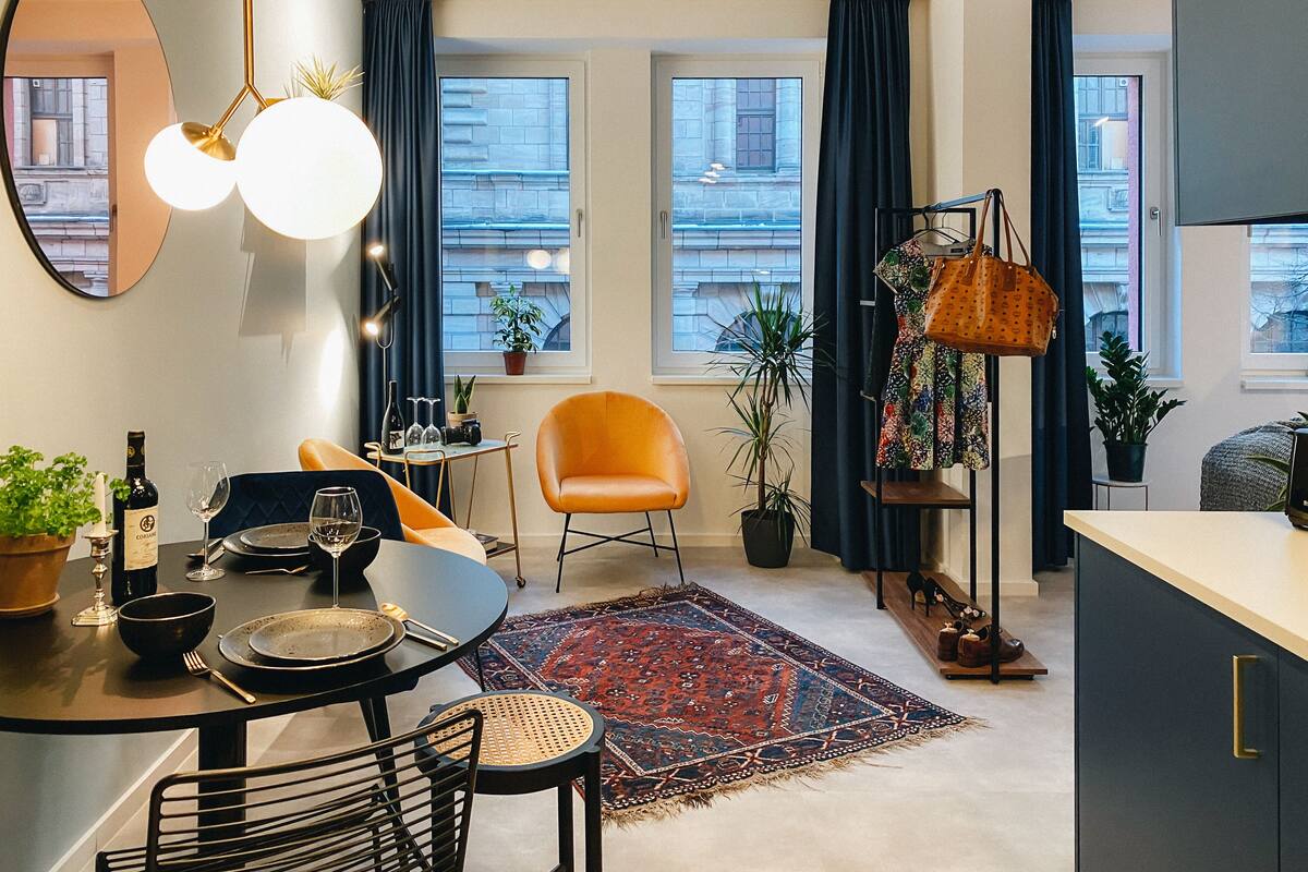 Un appartement moderne doté d’un coin repas, d’un grand miroir, d’une plante en pot, d’un tapis coloré et offrant une vue sur la ville grâce à de grandes fenêtres.