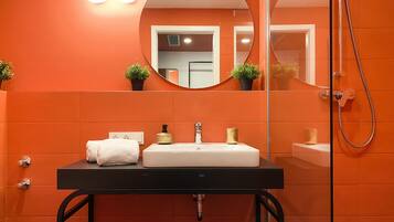 Ein Badezimmer mit einer orangefarbenen Wandfliese, einem schwarzen Waschbecken mit goldfarbenem Wasserhahn, einem weißen Handtuch und einem Spiegel mit rundem Rahmen.
