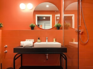 A bathroom with an orange tiled wall, a black sink with a gold faucet, a white towel, and a mirror with a round frame. - Astoria Apartments (Nuremberg)