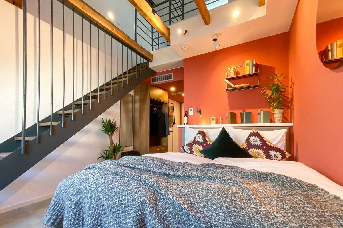 Une chambre à coucher avec un lit, un escalier et une étagère contenant des livres et des plantes.
