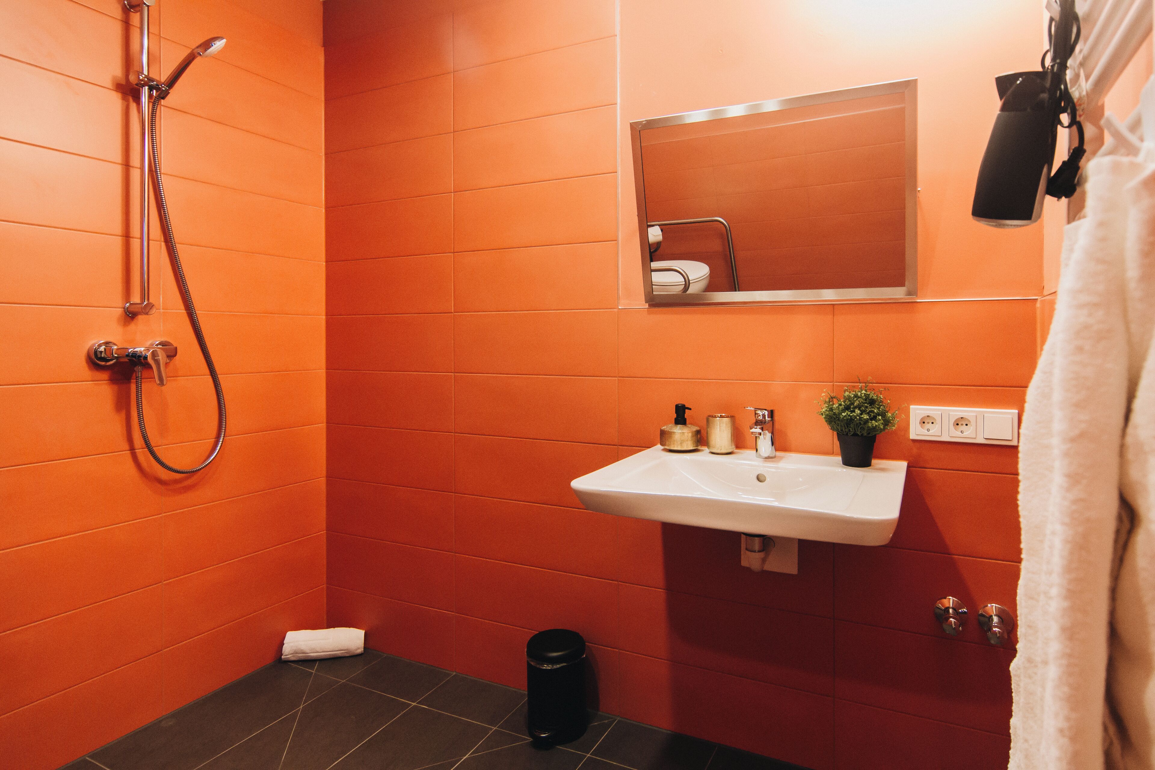 Ein Badezimmer mit orangefarbenen Wänden, einem weißen Waschbecken, einem Spiegel und einer Dusche.