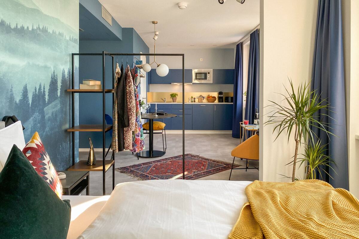 Une chambre d’hôtel moderne comprenant un lit, un bureau, un coin cuisine et un espace de vie.