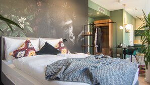 A modern bedroom with a large bed, a wardrobe, a desk, and a green wall. - Astoria Apartments (Nuremberg)
