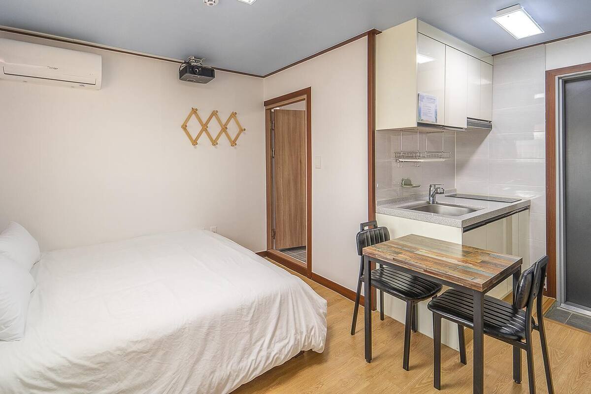 A compact bedroom with a bed, bedside table, and a small kitchenette with a sink and stove.