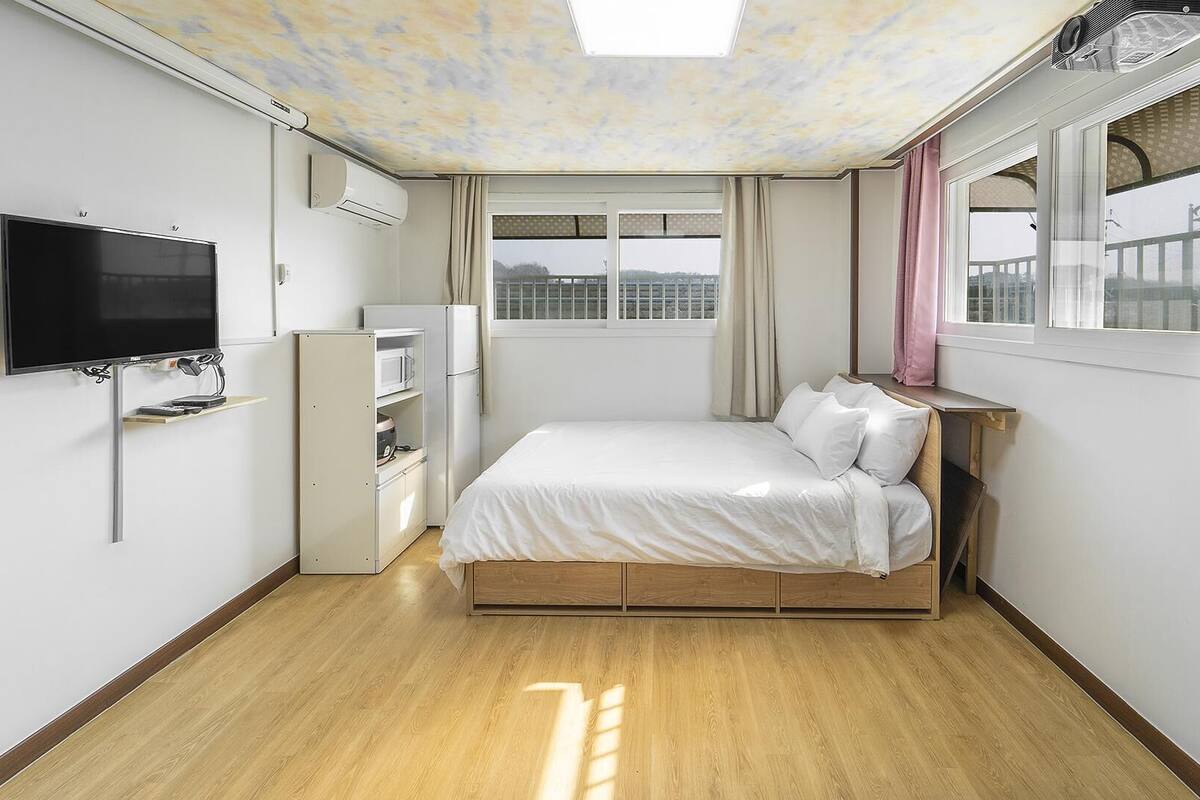 A bedroom with a bed, a TV, a wardrobe, and a window with curtains.