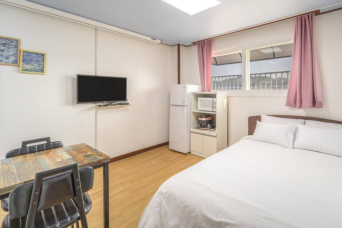 A compact hotel room with a bed, a desk with a chair, a television, a microwave, and a refrigerator.