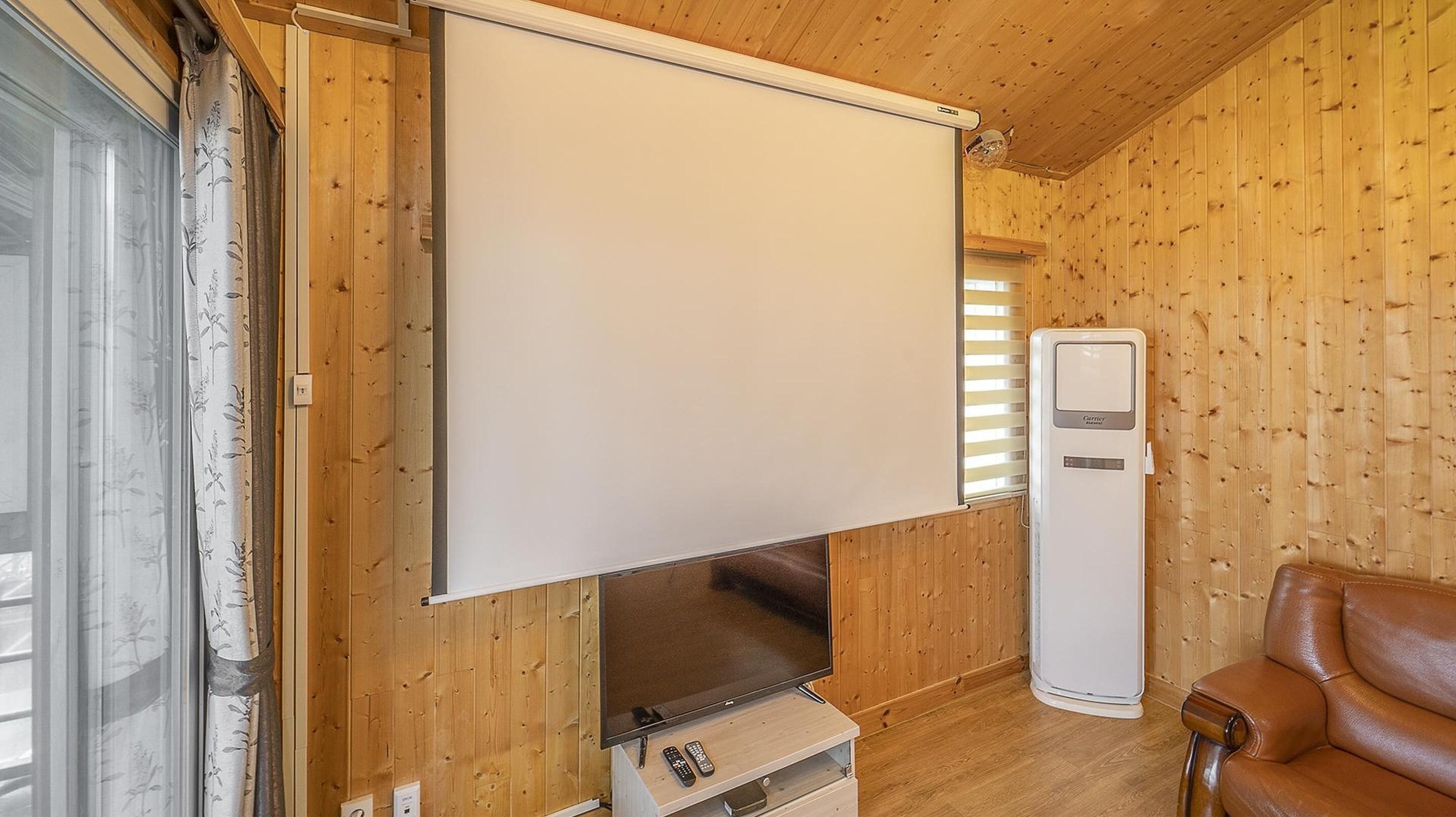 Habitación con una amplia televisión de pantalla plana montada en una pared de madera, un mueble de madera y un sofá de cuero.