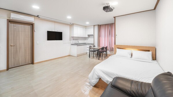 Habitación de hotel con cama, escritorio, silla, televisor y kitchenette.