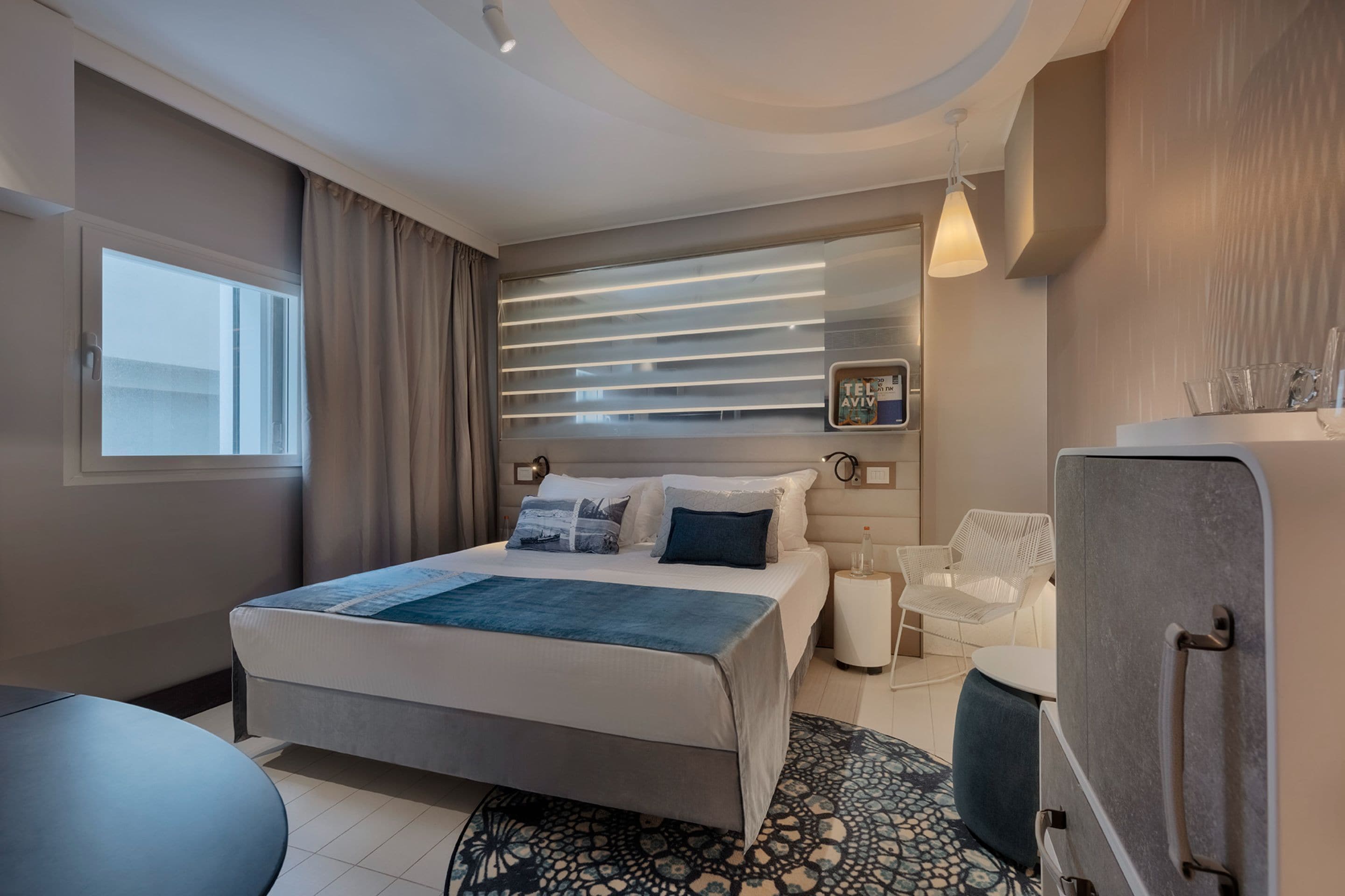 Une chambre d’hôtel moderne, dotée d’un grand lit, d’une petite table, d’une chaise, d’un bureau et d’une fenêtre avec des rideaux.
