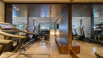 Un gimnasio moderno con máquinas de cardio, equipo de pesas y un banco de madera.