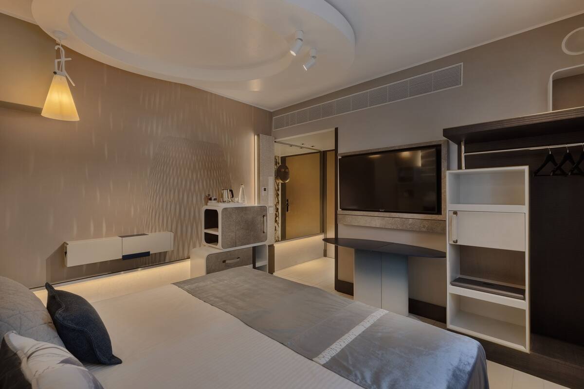 A modern hotel room with a large bed, a TV, a wardrobe, and a mirror.