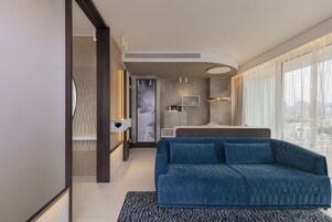 A modern bedroom with a large bed, a blue sofa, and a city view.