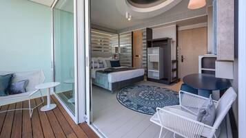 Habitación de hotel moderna con cama, una mesita redonda pequeña, una silla blanca, un sofá y un ventanal grande.
