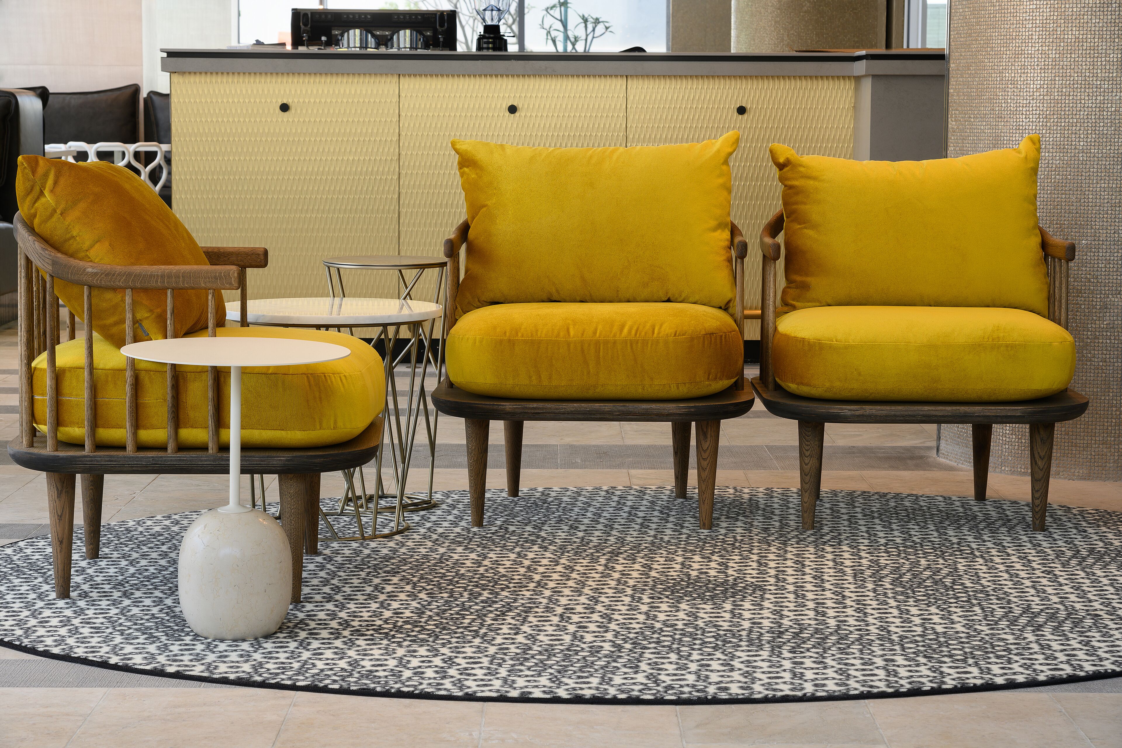 Een zithoek met twee gele stoelen en een kleine ronde tafel, een witte vaas en een tapijt met een patroon.