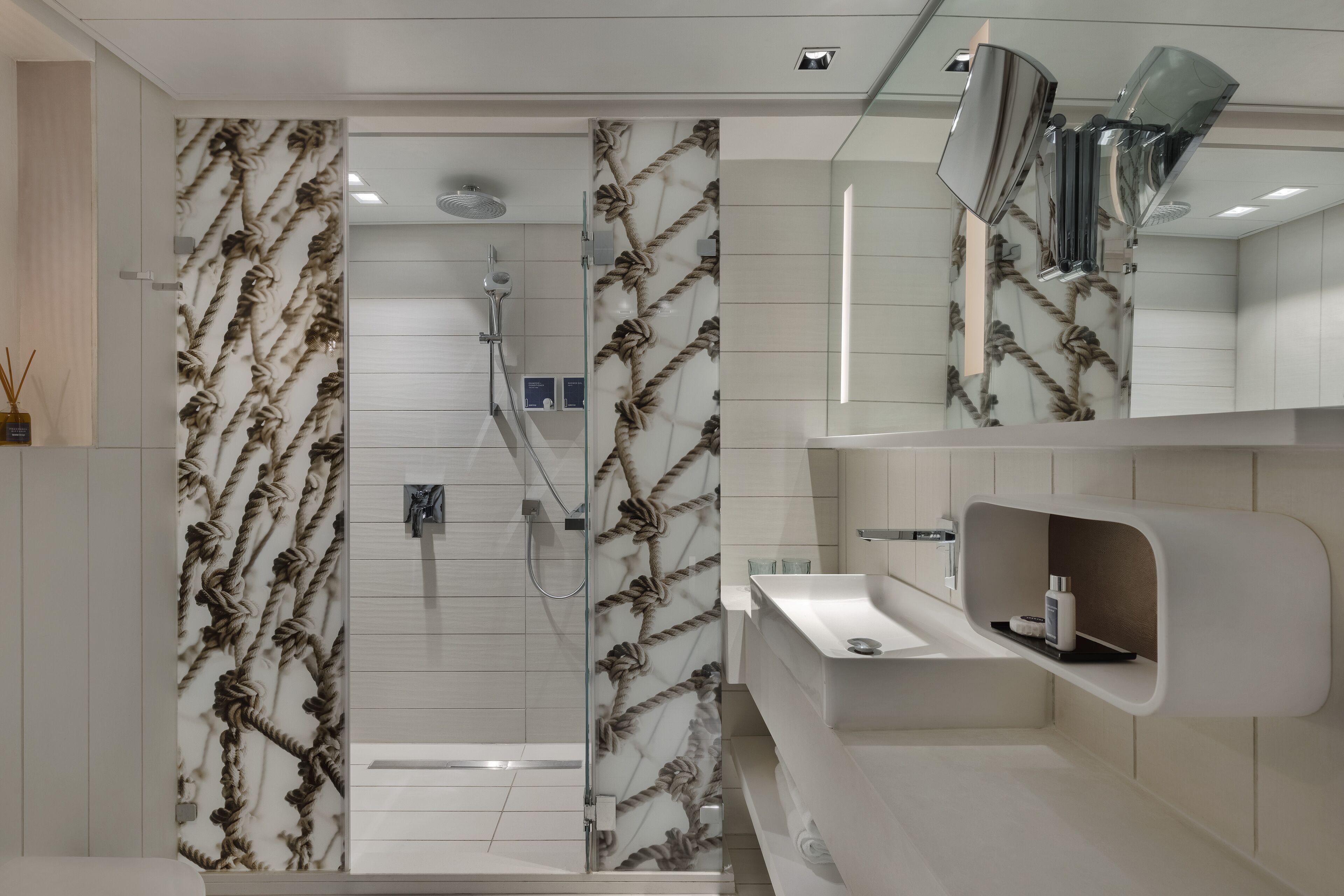 Ein modernes Badezimmer mit einer in Glas abgeschlossenen Dusche, Marmorwandverkleidungen und einem integrierten Waschbecken mit Spiegel darüber.