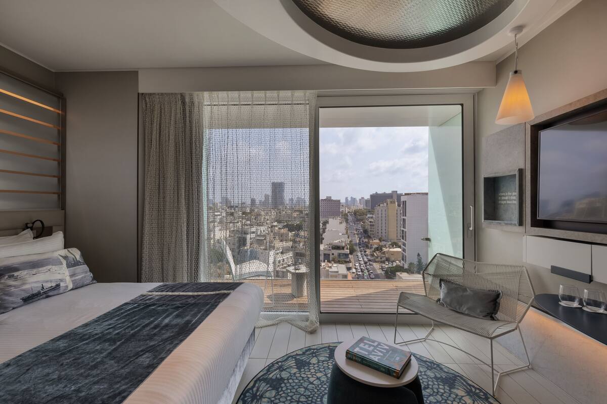 A modern hotel room with a large bed, a seating area with a view of the city, and a television mounted on the wall.