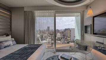 A modern hotel room with a large bed, a seating area with a view of the city, and a television mounted on the wall.