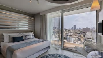 Camera da letto moderna con un letto grande, vista sulla città e un balcone con una sedia e un tavolo.