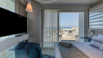 Een moderne hotelkamer met een groot bed, een flatscreen-tv, een kleine tafel en uitzicht op de stad en zee.