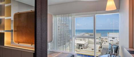 A modern hotel room with a large window offering a view of the sea and buildings.