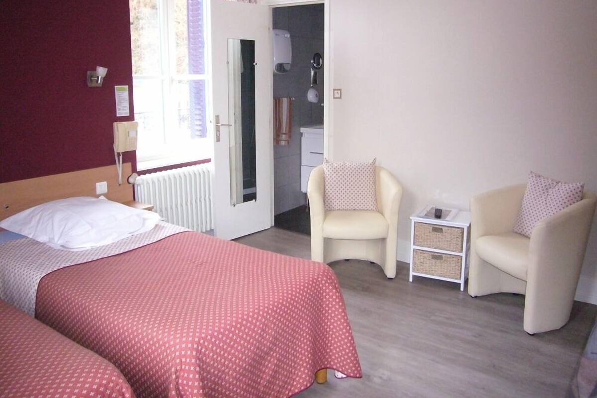 Habitación de hotel con dos camas, un área de descanso con dos sillones, una mesita y un radiador.
