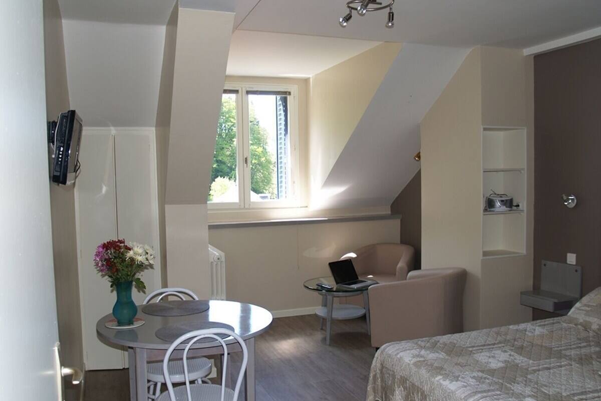 Una habitación compacta con una cama, una mesita con una laptop, una silla y una ventana que da a zonas verdes.