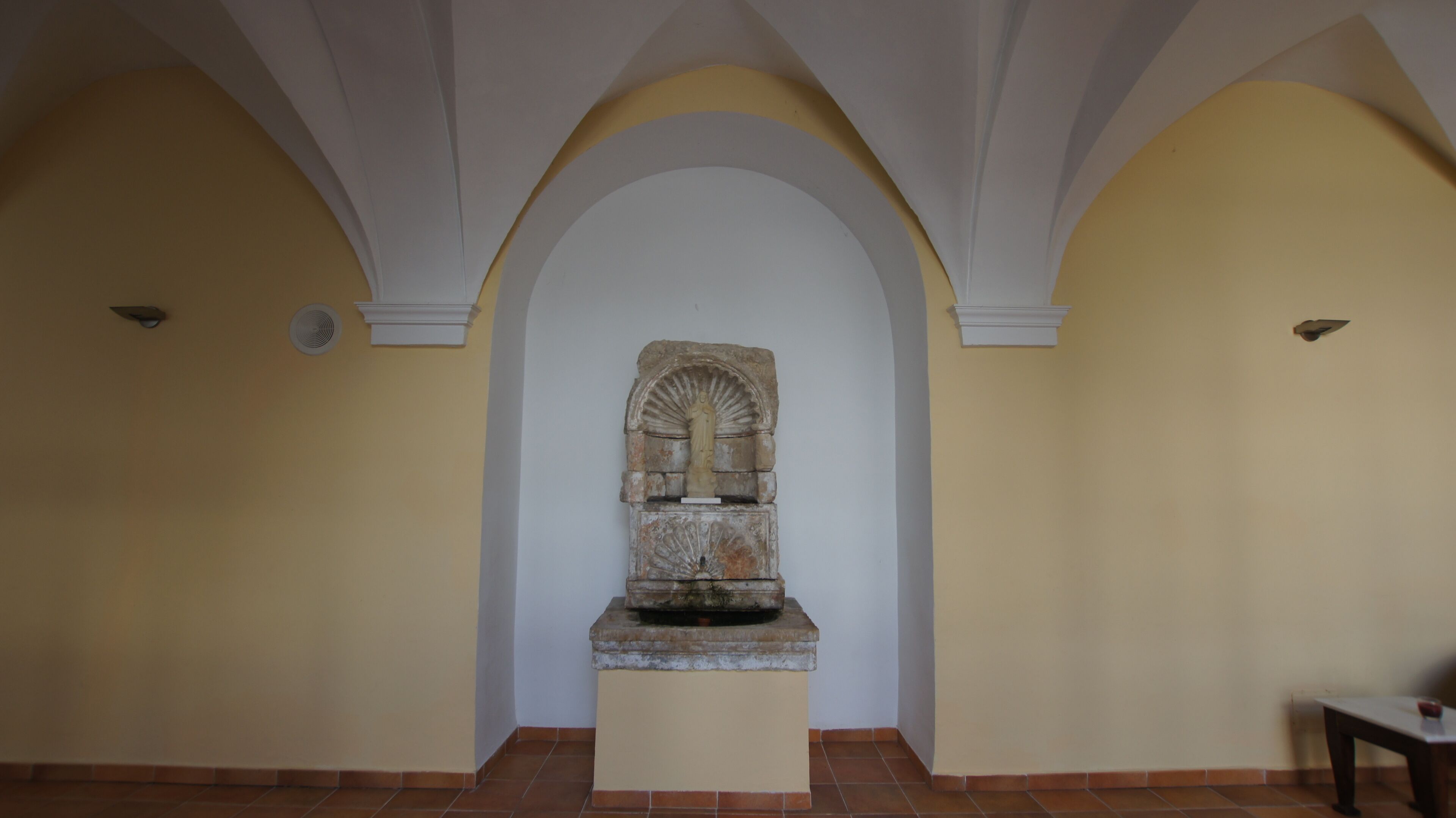 Una habitación con una escultura de piedra central, arcos blancos y piso de baldosas.