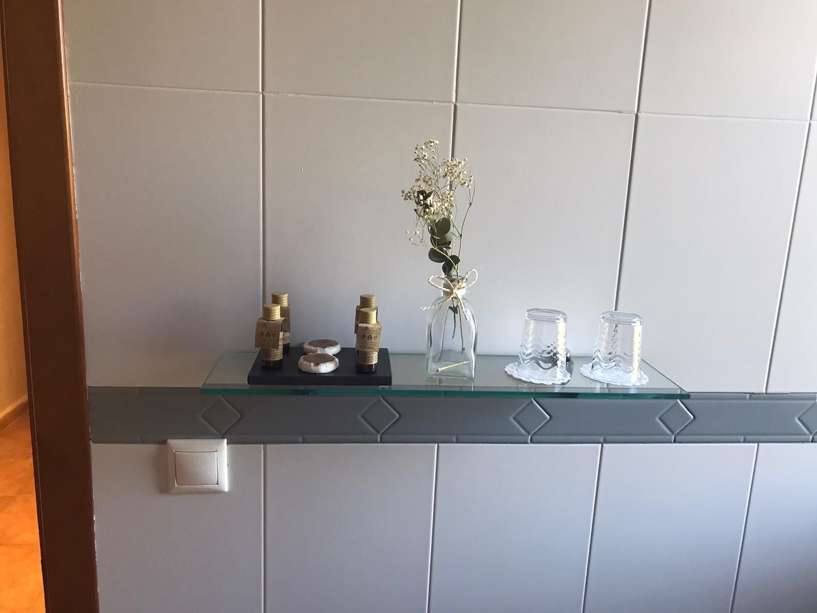 Un baño con un estante de vidrio que sostiene artículos de aseo y un florero con flores.