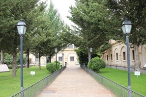 A pathway flanked by trees and lamp posts leading to a building with arched windows. - Hotel Monasterio de Tejeda (Garaballa)