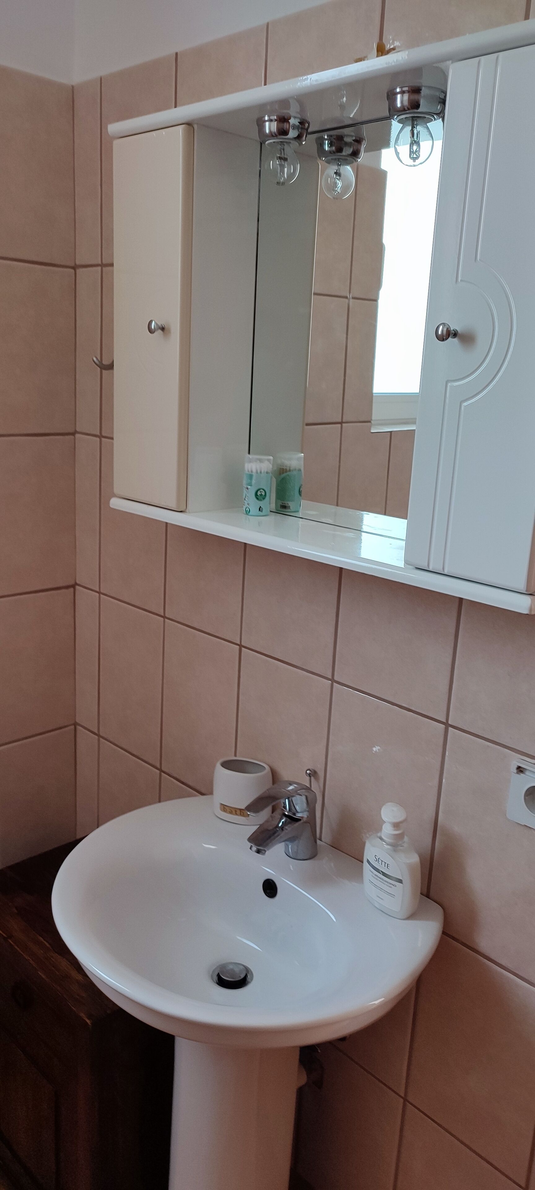 A bathroom with a white sink, a mirror above it, and a cabinet below.
