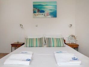 A hotel room with a bed, two pillows, a painting of a coastal scene, a ship's wheel decoration, and a small table with a cup. - Mili's House SeaView - Kalyves (Apokoronas)