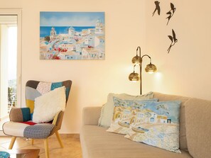A living room with a sofa, a chair, and a painting of a coastal town. - Mili's House SeaView - Kalyves (Apokoronas)