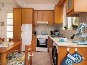 A compact kitchen with wooden cabinets, a white refrigerator, a stove, a washing machine, and a sink. - Mili's House SeaView - Kalyves (Apokoronas)