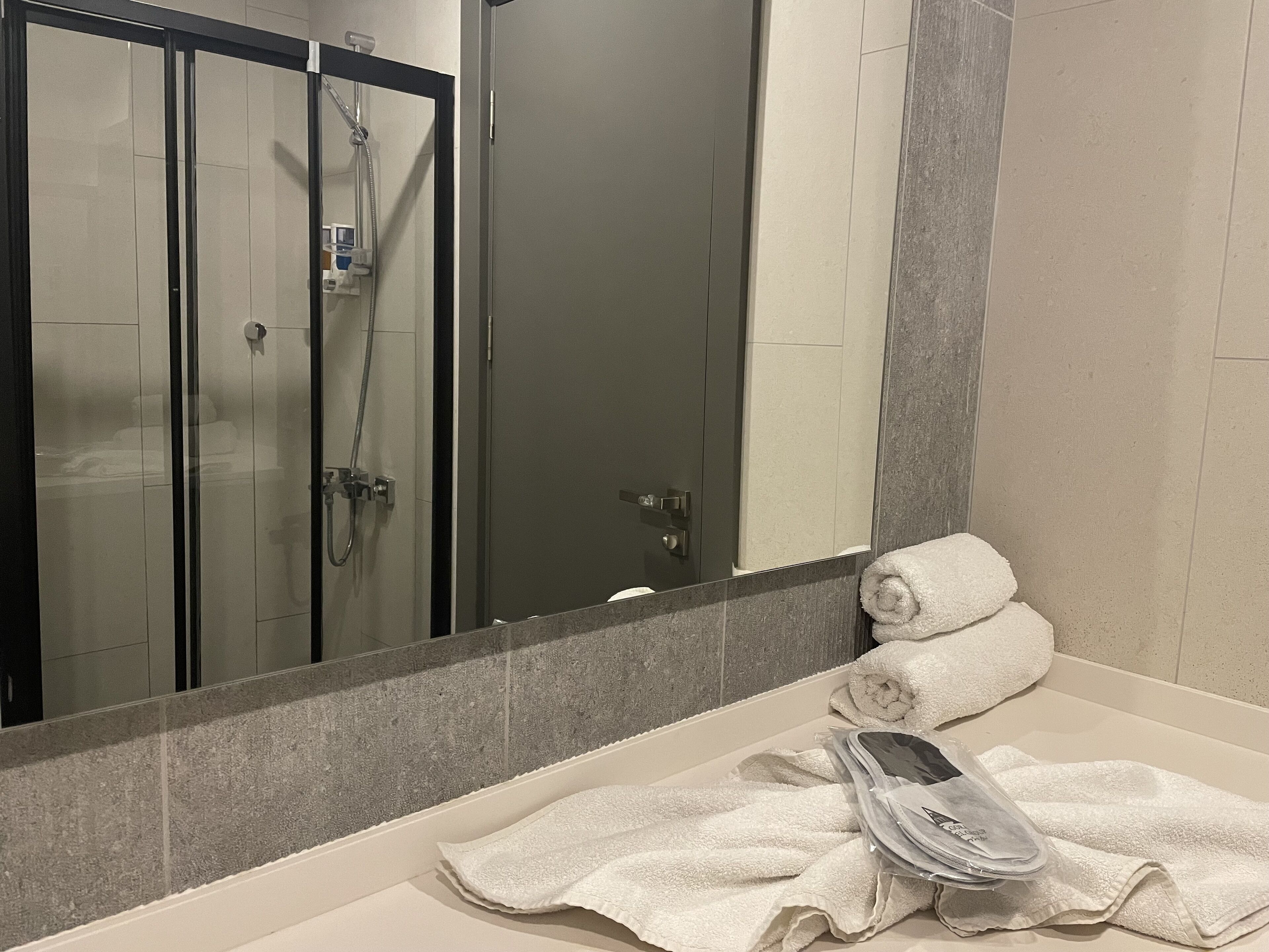 A bathroom with a glass-enclosed shower, a mirror, and a sink with towels and toiletries.