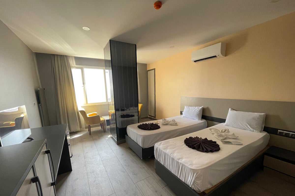 A hotel room with two beds, a desk, a chair, and a large window.