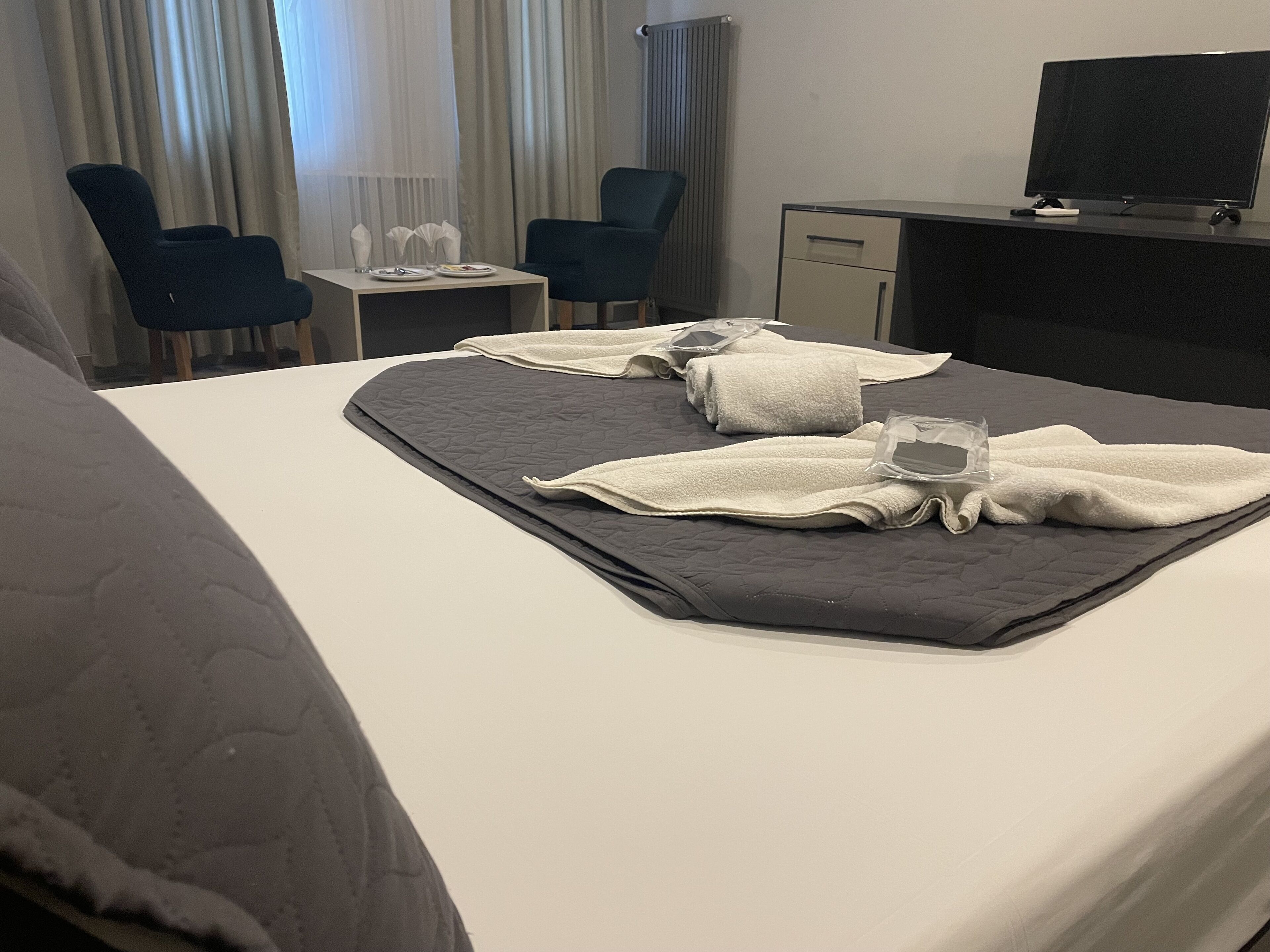A hotel room with a bed, two chairs, a small table with a glass, and a TV.