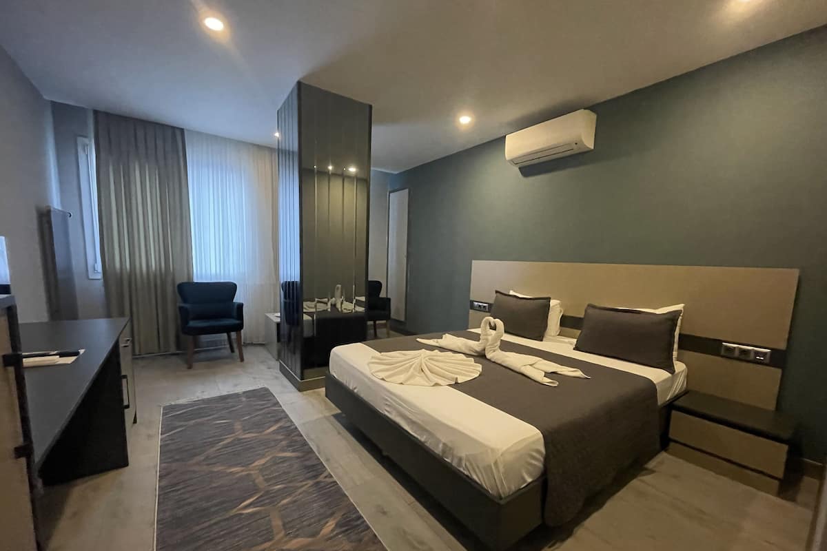 A modern hotel room with a large bed, a desk, a chair, and a mirror.